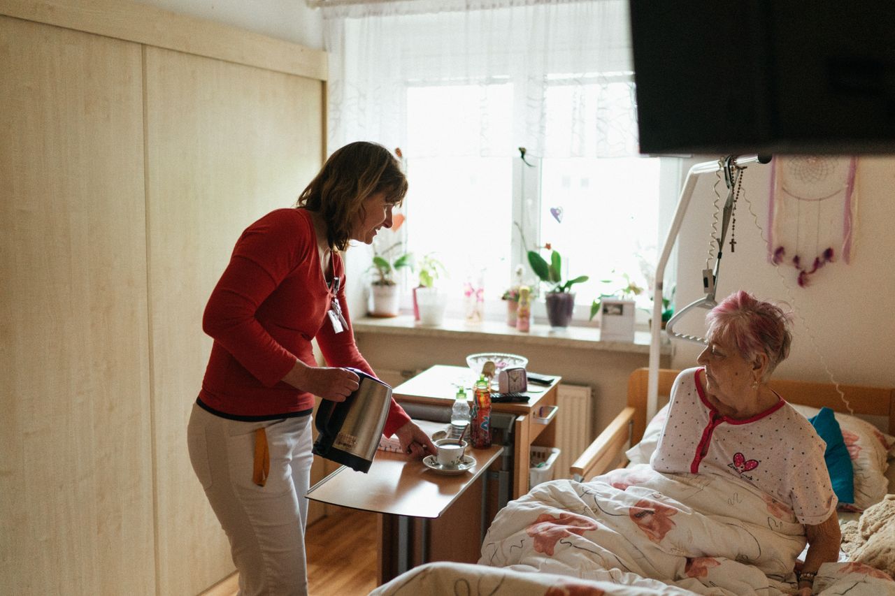 Mastering the First Impression: Your intriguing post title goes here A caregiver serves tea to a senior woman in a cozy bedroom setting, fostering comfort and care.