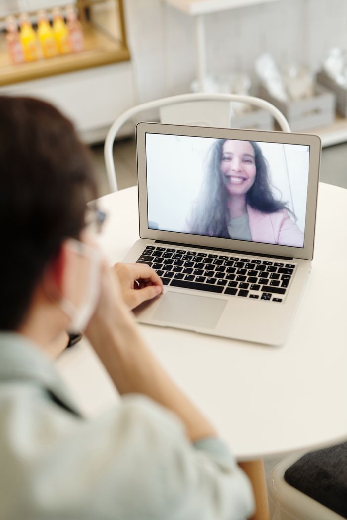 Close-up of a video call showing a smiling woman on a laptop screen in a cozy indoor setting.