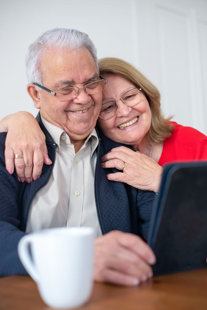 Features Happy senior couple smiling while making a video call at home, connected and joyful.